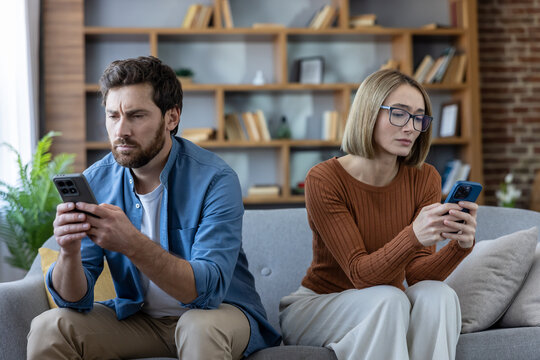 Couple sitting on a couch at home ignoring each other while engrossed in their smartphones, illustrating communication breakdown and technology addiction in relationships