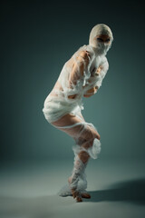 Obraz premium Conceptual portrait of a person wrapped like a mummy in white bandages, struggling in a constrained pose.