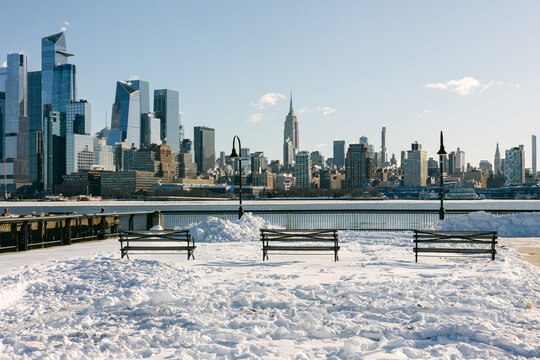 Snow covers the ground as benches sit empty near the waterfront in New York City on a winter day