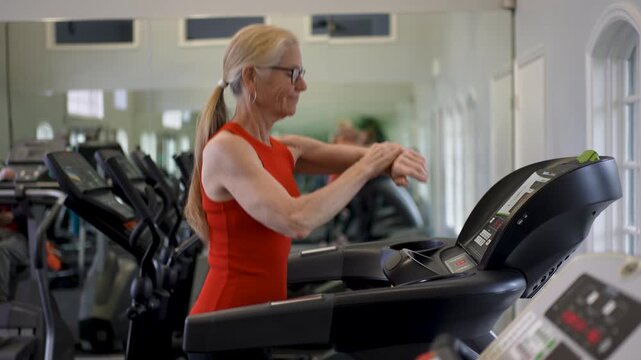 Mature woman works out on a treadmill in a gym setting focused on health and fitness. She commits to her workout routine.