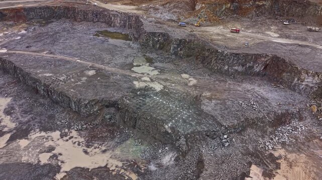 Large granite quarry with heavy machinery working on the site. Workers are present, and vehicles are moving material in the area. Ground is rocky and uneven.