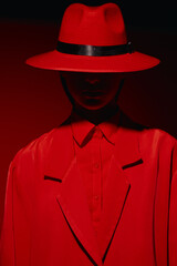 Mysterious fashion model wearing an oversized red suit and wide-brimmed hat with a shadowed face....