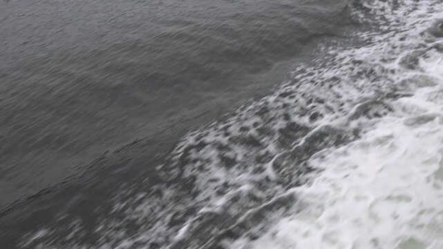 Tracking along edge of bow wake in dark ocean viewed from above as ship creates flowing pattern in water