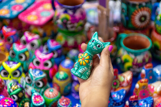 A hand holds a colorful, handcrafted ceramic cat figurine