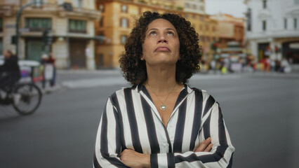 Hispanic middle aged woman in striped shirt stands with arms crossed on city street under overcast sky  defiance. © Krakenimages.com