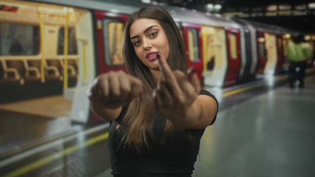 Woman showing middle finger with hands extended toward camera on subway platform beside stopped train; defiance attitude.