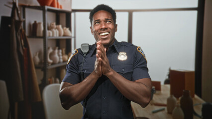 Naklejka premium Man in police uniform claps hands in pottery studio while smiling and laughing with radio mic on shoulder and visible badge; joy celebration.