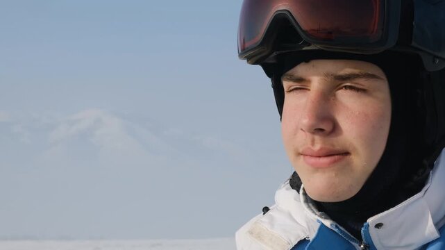 Portrait of young skier in helmet with goggles lifted on top, looking calmly and confidently into distance anticipating downhill. Teenage snowboarder gazing with happiness. Copy space.