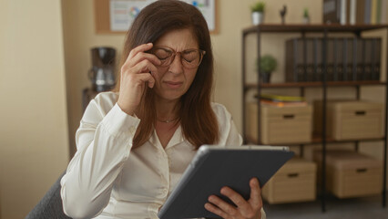 Woman touching forehead with her hand and holding a digital tablet at a desk in a sunlit office  stress. © Krakenimages.com