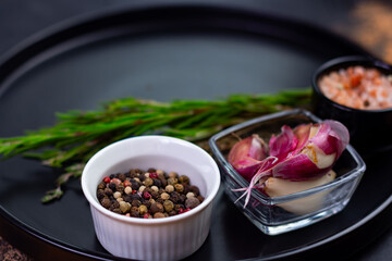 Different types of spices and herbs displayed on a black plate in a kitchen setting during daylight