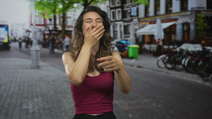 Fototapeta premium Woman in red tank top laughing and pointing finger on vibrant bustling cobblestone street at camera; joy.