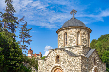  Stone orthodox church in Romanian countryside with Bran ( Dracula ) castle at the background   
