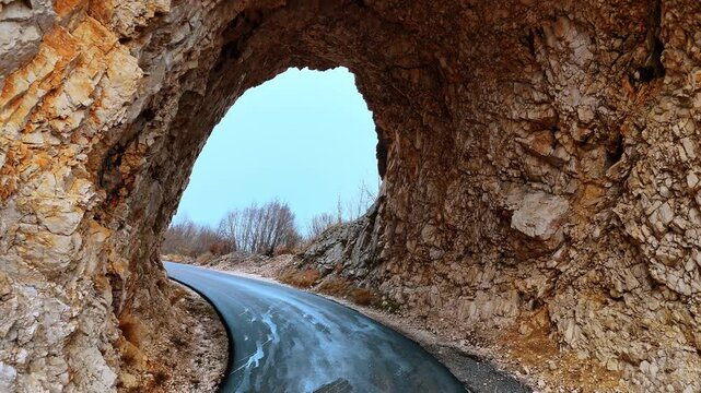 Passing through the tunnel in the rock. Multiple trees with no foliage grow on the mountains. Winter in Montenegro.