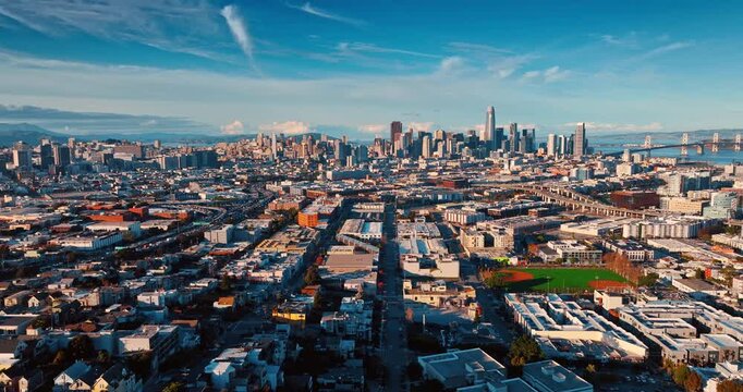 Dense urban landscape of San Francisco lit by the setting sun. Drone footage approaching the gorgeous downtown of the city with high-rise architecture.