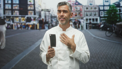 Man chef in white coat holds a cleaver in his right hand with left hand pressed to chest while...