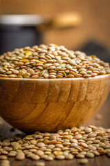 Uncooked green lentil in bowl on wooden table.