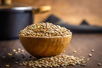 Uncooked green lentil in bowl on wooden table.