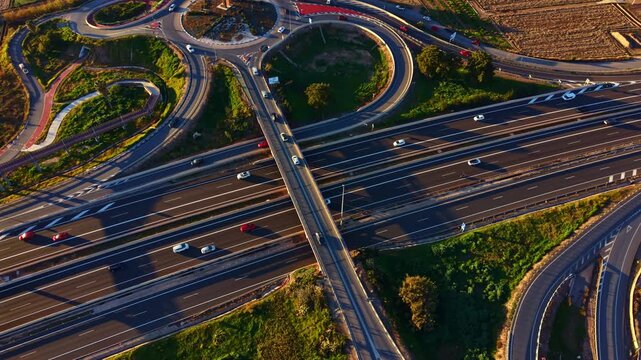 Vehicles move along multiple roadways in an urban setting with roundabouts and green areas. The view shows the layout of the roads from above on a clear day.