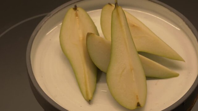 Slices of pear arranged on a white plate, showcasing the fresh fruit's texture and color in a well-lit kitchen setting
