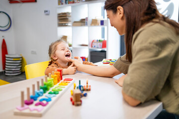 Speech therapist guiding a smiling preschool girl through playful articulation exercises with a colorful wooden toy to build communication, confidence, and early language skills