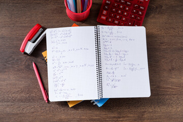 Homework. Notebook with math formulas and different stationery on wooden table, flat lay