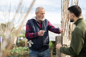 Man quarrels with mature male neighbor in suburban area garden. Ill-wishers, complaints and...