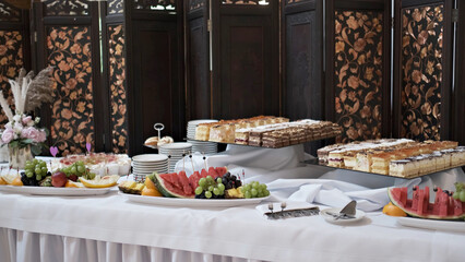 Fototapeta premium Elegant dessert buffet table featuring platters of fresh fruit and assorted sliced cakes at an event