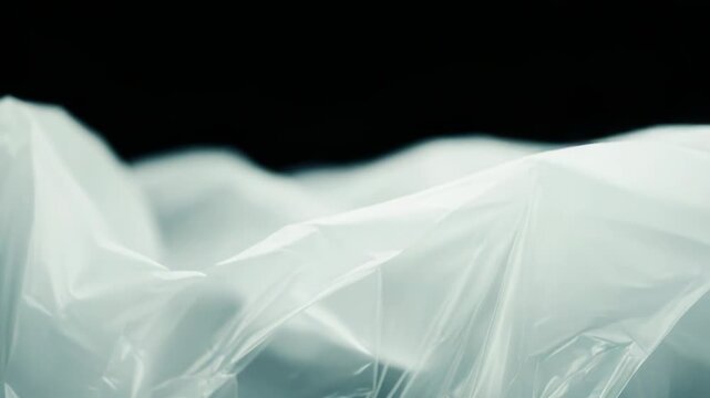 Transparent crinkled plastic with soft folds and creases forming an abstract luminous background, reflecting light and casting gentle shadows for a modern minimal texture