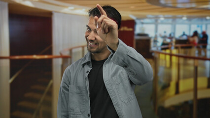 Fototapeta premium Young man smiling confidently in a modern hotel lobby, pointing forward with a friendly gesture, capturing an inviting atmosphere indoors with warm lighting.