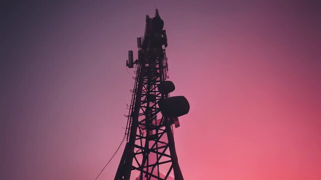 Telecommunication tower, rich in antennae, stands silhouetted against a beautiful gradient sky during sunset, symbolizing global connectivity and modern wireless technology infrastructure