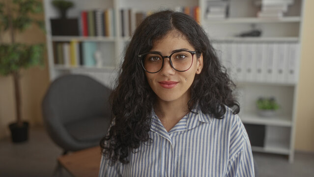 Woman wearing glasses with eyes closed and small cheek piercings smiling in building; calm contentment introspection.
