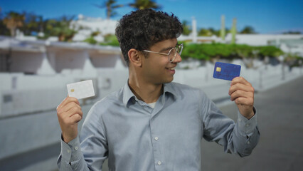Man holding two plastic credit cards upright on a sunlit city street near white building facade  financial choice. © Krakenimages.com