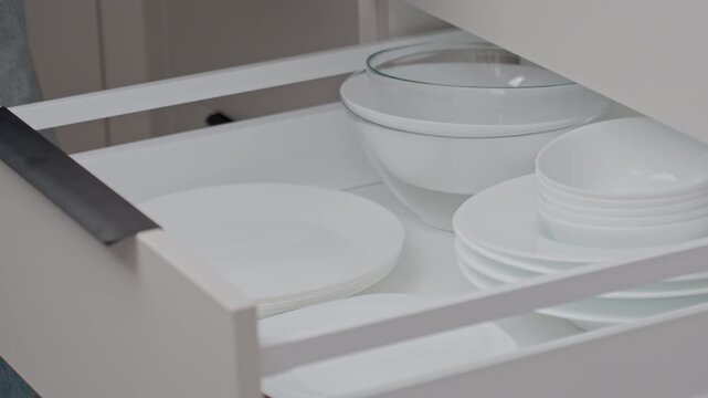 Close up of woman hand putting white plates into kitchen drawer with bowls and dishes. Concept of kitchen organization