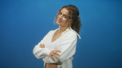 Woman with arms crossed wearing white hoodie and crop top with hoop earrings, smiling in a studio  confidence ease. © Krakenimages.com
