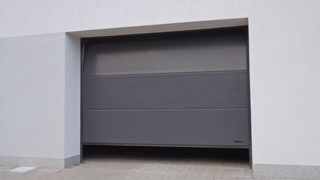 Hand presses remote control while holding house keys in front of residential garage door. Concept of automated home access