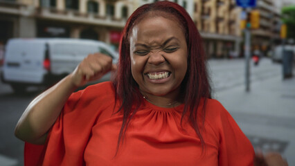 Fototapeta premium Woman in orange top holding up three fingers near crosswalk on busy city street; confidence empowerment.