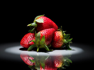 strawberries in a circle of white light on a black background with reflection in the shiny ground