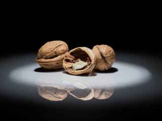 walnuts in a circle of white light on a black background with reflection in the shiny ground