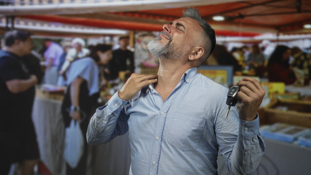 Man holding car keys and rubbing his neck at a crowded street market souvenir stall; discomfort during errands.