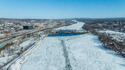 Aerial view of frozen Hudson River in Albany, New York, with bridges, highways, and snowy riverbanks in winter.