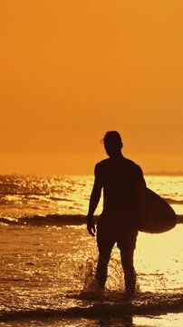 Surfer walking out of ocean at golden sunset