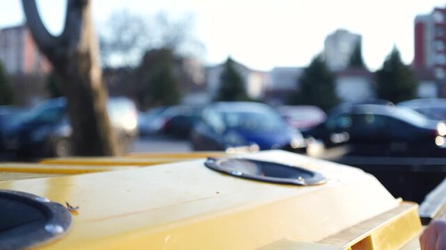 A woman hand throwing  a plastic bottle into the recycling trash can outdoors, closeup