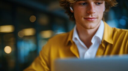 A young man is sitting at a table with a laptop in front of him