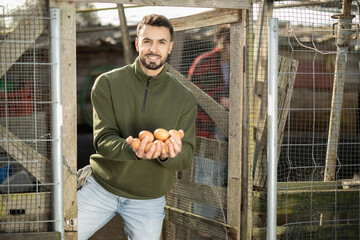 Man holding fresh eggs in a chicken coop © JackF