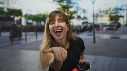 Woman blows a kiss with hand to lips while holding a game controller on a city street  playful greeting. © Krakenimages.com