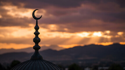 Fototapeta premium Serene silhouette of a mosque's crescent moon finial at sunset against a mountainous landscape with cloudy sky