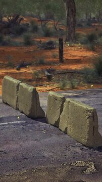 A row of rugged stone blocks sits on a dusty road, surrounded by arid terrain and scattered shrubs.