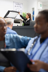 Asian female healthcare staff member scans medical forms using copy machine. Hospital administrator...