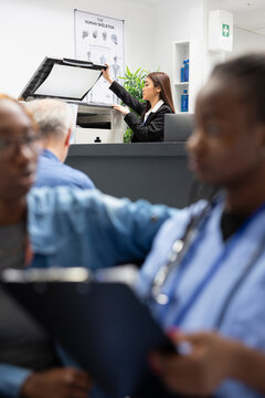 Asian female healthcare staff member scans medical forms using copy machine. Hospital administrator manages document printing and faxing tasks for efficient coordination between patients and doctors.
