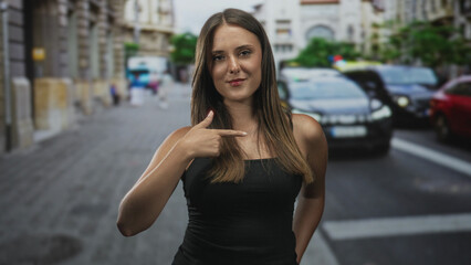Fototapeta premium Woman points finger to chest, bare shoulders visible in busy street with cars, buildings and a crosswalk; confidence adventure.